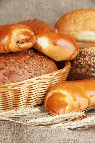 Baked bread in wicker basket on burlap background — Stock Photo, Image
