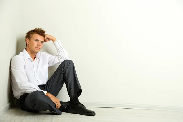 Young businessman sitting on floor, on gray wall background — Stock Photo, Image