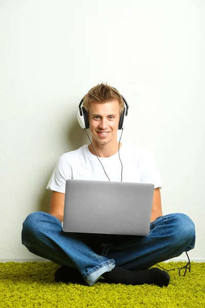 Hombre joven relajándose en la alfombra y escuchando música, sobre fondo gris de la pared — Foto de Stock