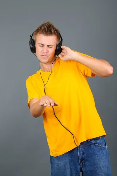 Joven guapo escuchando música sobre fondo gris —  Fotos de Stock