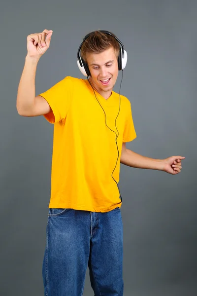 Bonito jovem ouvindo música em fundo cinza — Fotografia de Stock