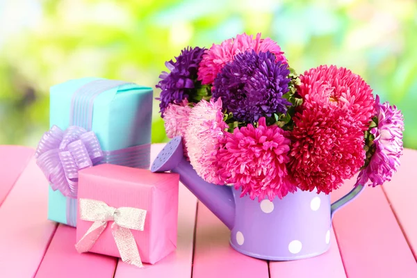 Gifts and flowers in watering can, on nature background — Stock Photo, Image