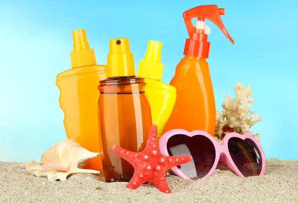 Botellas con crema bronceadora y gafas de sol, sobre fondo azul — Foto de Stock