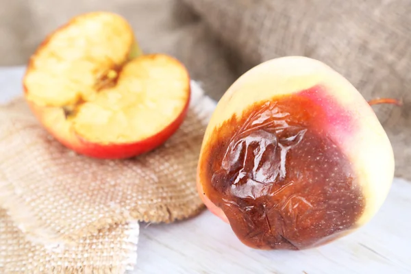 Rotten apples on wooden board on sackcloth — Stock Photo, Image