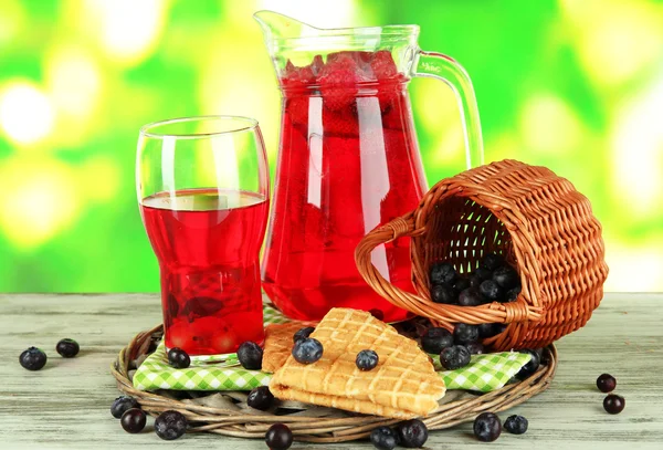 Pitcher and glass of compote on napkin on wooden table on nature background — Stock Photo, Image