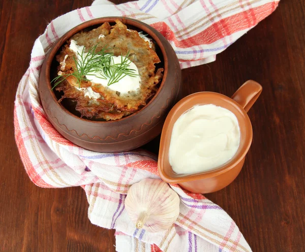 Potato pancakes in pot, on wooden background — Stock Photo, Image