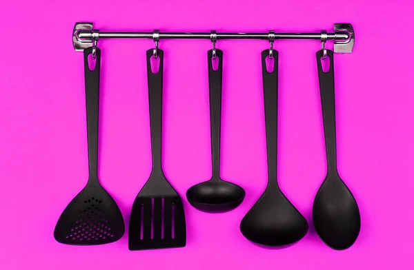 Черная посуда на серебряных крючках, на розовом фоне — стоковое фото