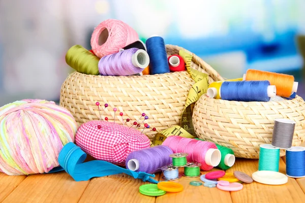 Wicker baskets with accessories for needlework on wooden table, on bright background — Stock Photo, Image