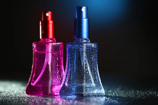 Women perfume in beautiful bottles on dark background with color light — Stock Photo, Image