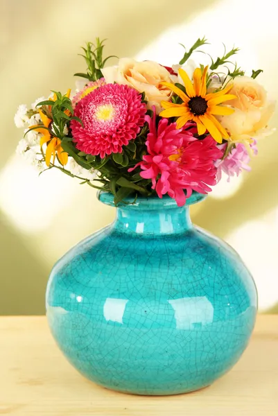 Beautiful bouquet of bright flowers in color vase, on wooden table, on bright background — Stock Photo, Image