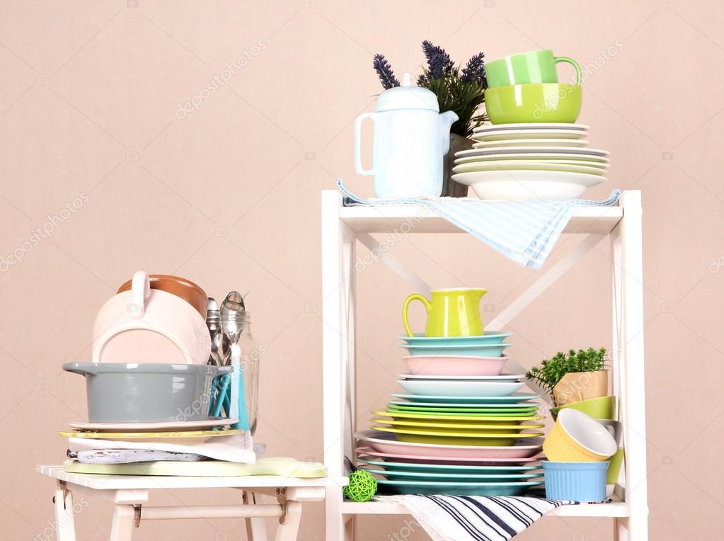 Beautiful white shelves with tableware and decor, on color wall background, close-up