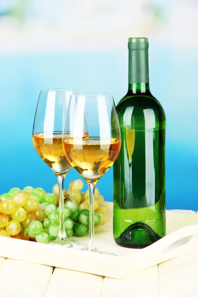 Uvas maduras, garrafa e copos de vinho na bandeja, no fundo brilhante — Fotografia de Stock