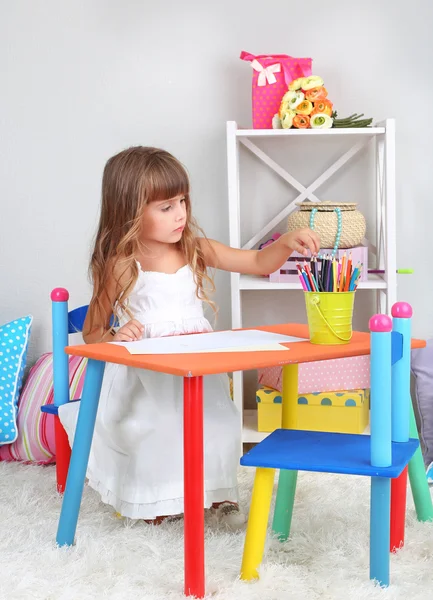 少女は、灰色の壁の背景の部屋のテーブルに座っているを描画します。 — ストック写真