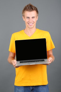 un joven guapo con portátil sobre fondo gris