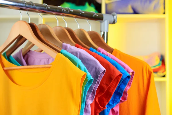 Verscheidenheid van casual t-shirts op houten hangers op planken achtergrond — Stockfoto
