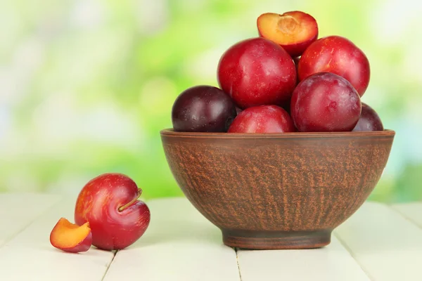 Ripe plums in bowl on wooden table on natural background — Stock Photo, Image