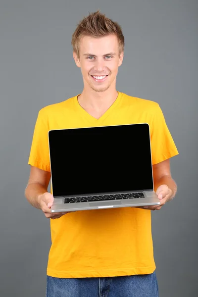 Un joven guapo con portátil sobre fondo gris — Foto de Stock