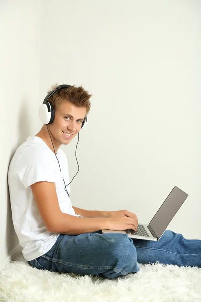 Молодой человек отдыхает на ковре и слушает музыку, на сером фоне стены — стоковое фото