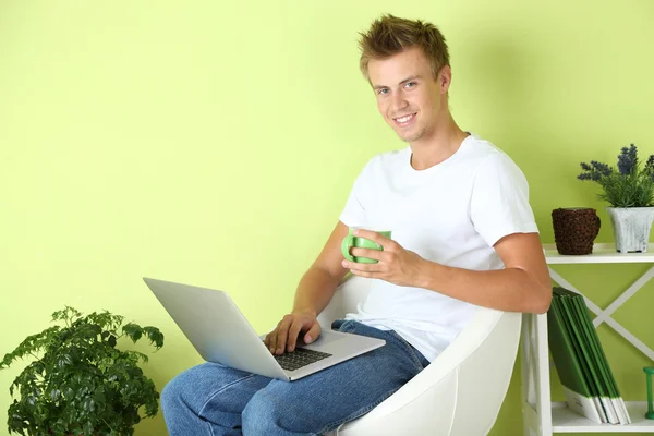 Young man relaxing with laptop in armchair, on home interior background — Stock Photo, Image