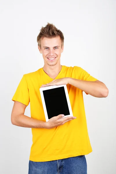 Pohledný mladý muž s tabletem na šedém pozadí — Stock fotografie