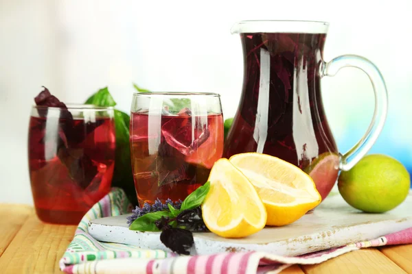 Red basil lemonade in jug and glass, on wooden table, on bright background — Stock Photo, Image