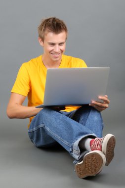 un joven guapo con portátil sobre fondo gris