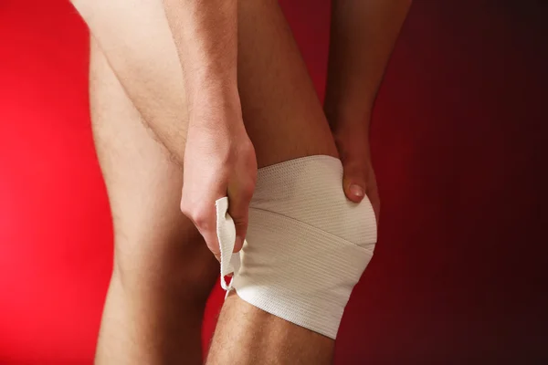 Young man with elastic bandage on knee, on red background — Stock Photo, Image