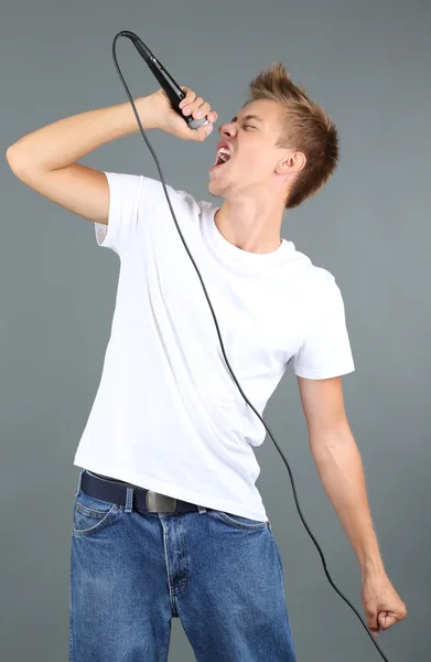 Handsome young man sings on grey background — Stock Photo, Image