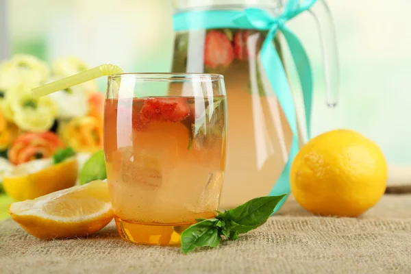 Basil lemonade with strawberry in jug and glass, on wooden table, on bright background — Stock Photo, Image