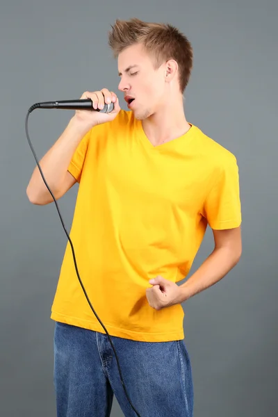 Przystojny młody mężczyzna śpiewa na szarym tle — Zdjęcie stockowe