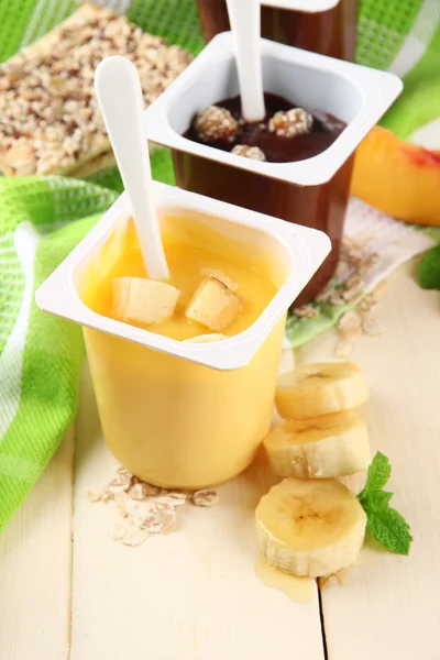 Sobremesas de creme saborosas com pedaços de frutas frescas, biscoitos e flocos, na cor de fundo de madeira — Fotografia de Stock