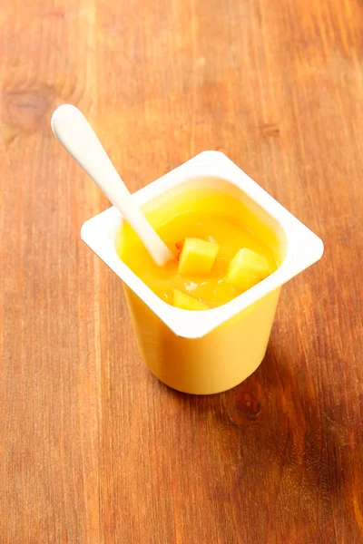 Вкусный йогурт в открытой пластиковой чашке на деревянном фоне — стоковое фото