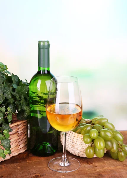 Uvas verdes e roxas maduras em cesta com vinho sobre mesa de madeira sobre fundo brilhante — Fotografia de Stock