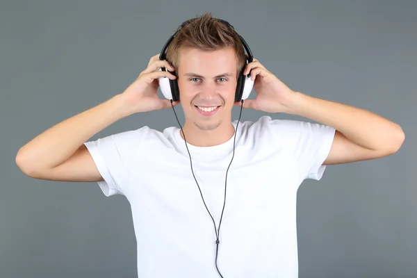 Joven guapo escuchando música sobre fondo gris — Foto de Stock