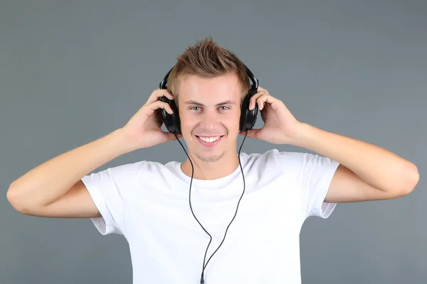 Bonito jovem ouvindo música em fundo cinza — Fotografia de Stock