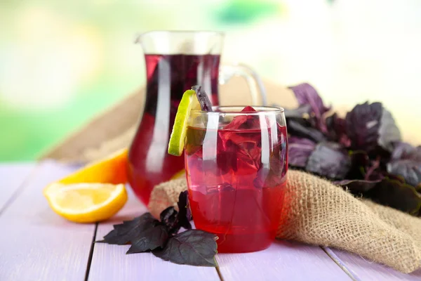 Red basil lemonade in jug and glass, on wooden table, on bright background — Stock Photo, Image
