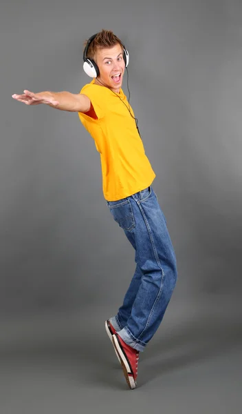 Joven guapo escuchando música sobre fondo gris — Foto de Stock