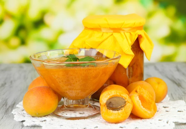 Apricot jam in glass jar and fresh apricots, on wooden table, on bright background — Stock Photo, Image