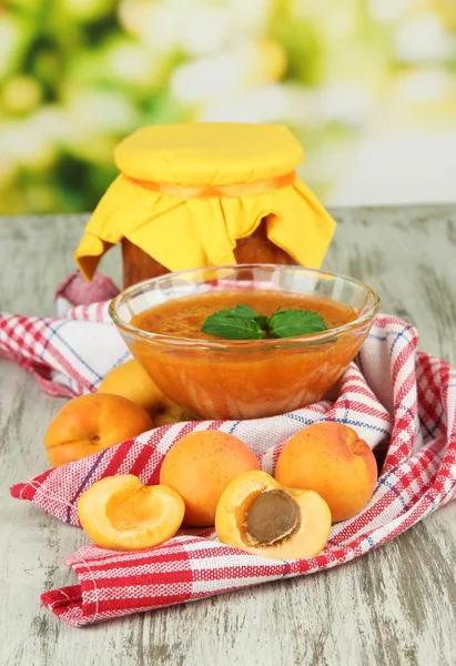 Confiture d'abricots dans un bol en verre et abricots frais, sur table en bois, sur fond lumineux — Photo