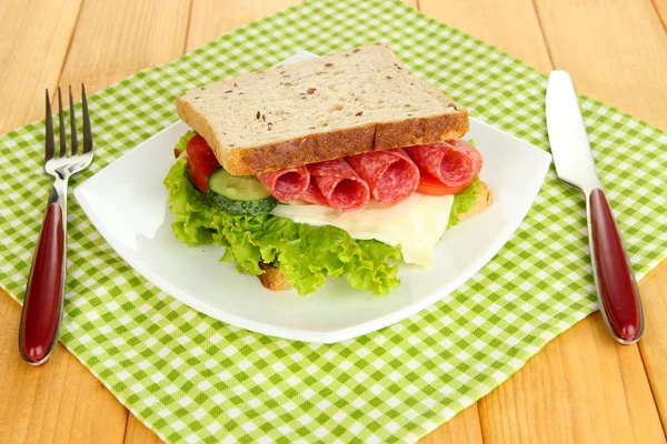 Sanduíche saboroso com salsicha de salame e legumes na placa branca, no fundo de madeira — Fotografia de Stock