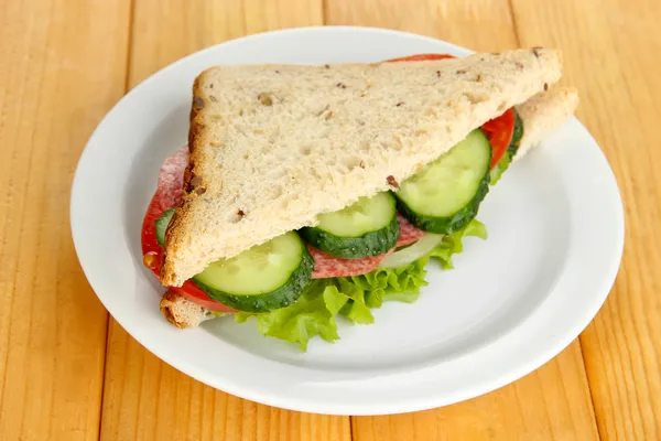 Смачний бутерброд з салямі ковбаса і овочі на білій тарілці, на дерев'яному фоні — стокове фото