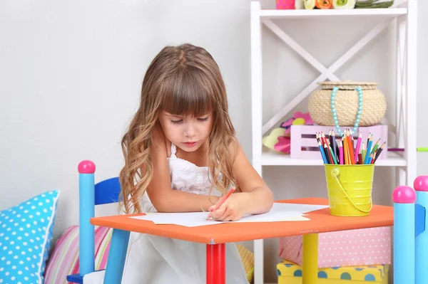 Little girl draws sitting at table in room on grey wall background — Stock Photo, Image