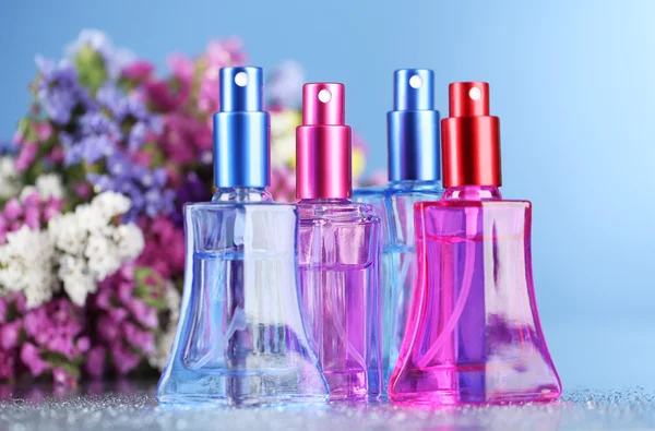 Perfume de mujer en hermosas botellas y flores sobre fondo azul —  Fotos de Stock