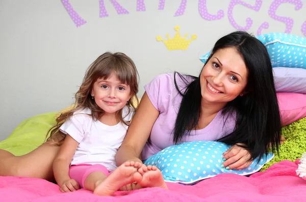 Kleines Mädchen mit Mutter auf Bett liegend im Zimmer auf grauem Wandhintergrund — Stockfoto