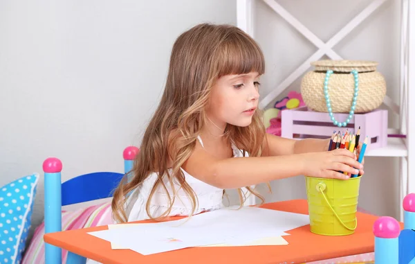 Menina desenha sentado à mesa no quarto no fundo da parede cinza — Fotografia de Stock