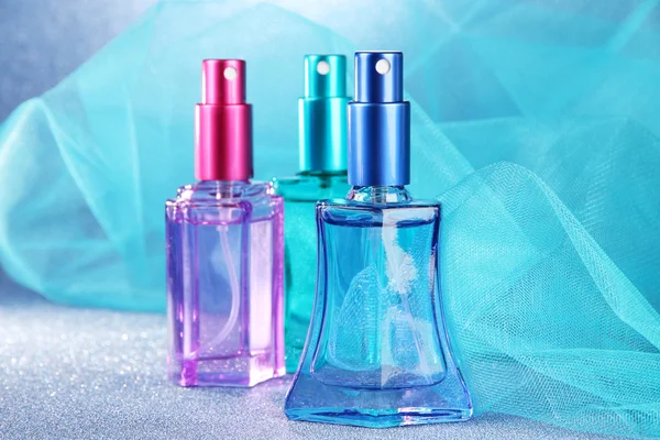 Perfume de mujer en hermosas botellas sobre fondo azul — Foto de Stock