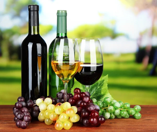 Wine bottles and glasses of wine on bright background — Stock Photo, Image