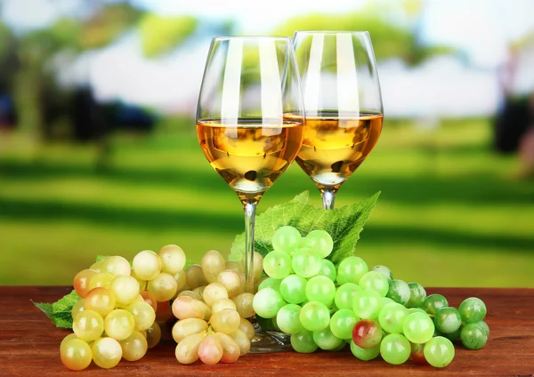Ripe grapes and glasses of wine, on bright background — Stock Photo, Image