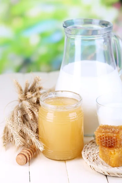 Miel et lait sur table en bois sur fond naturel — Photo