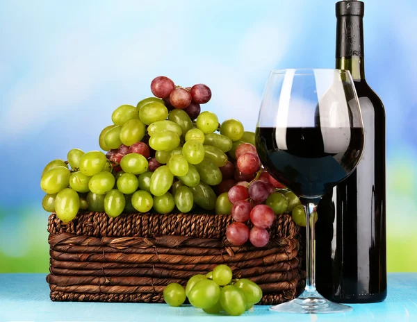 Uvas maduras verdes y moradas en canasta con vino sobre mesa de madera sobre fondo natural — Foto de Stock